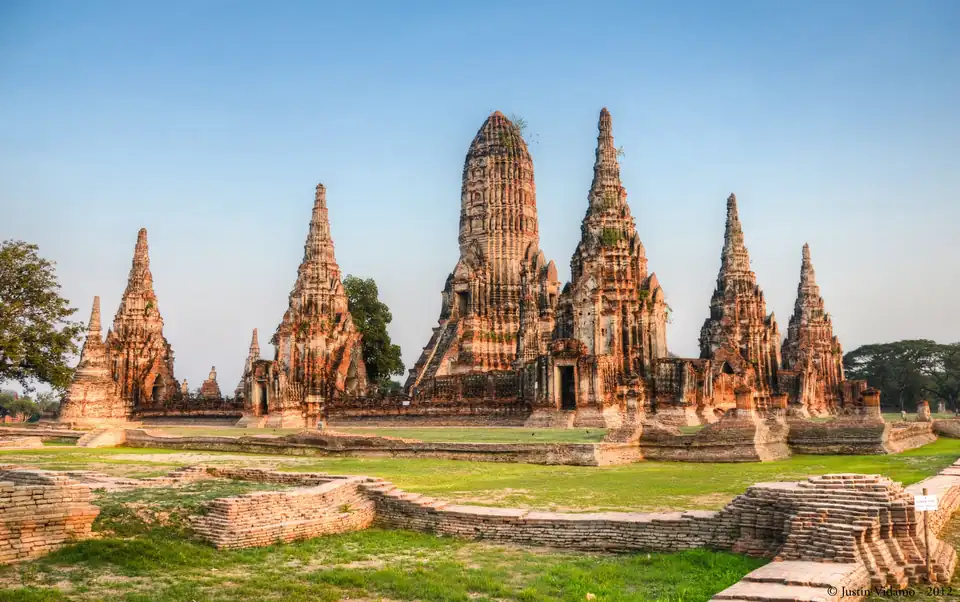 The central prang and surrounding chedis of Wat Chaiwatthanaram silhouetted against an orange sunset