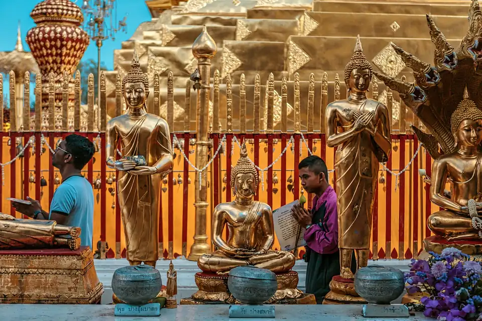 Gilded Buddha images in different postures on a temple terrace, each with a small label, in front of a gold-plated chedi