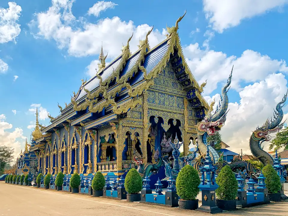 The cobalt and gold exterior of Wat Rong Suea Ten with naga guardians at the steps