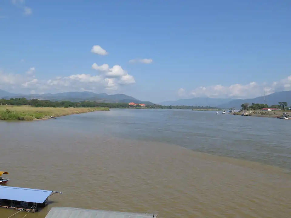 A wide brown river meeting a greener one below low forested hills, seen from a viewpoint