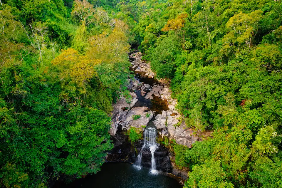 Aerial view of Khlong Chao waterfall dropping into a dark pool surrounded by dense jungle