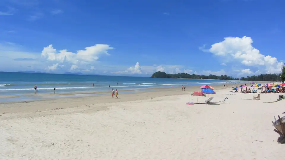 A wide flat beach on Koh Lanta with parasols, a few swimmers and a green headland in the distance