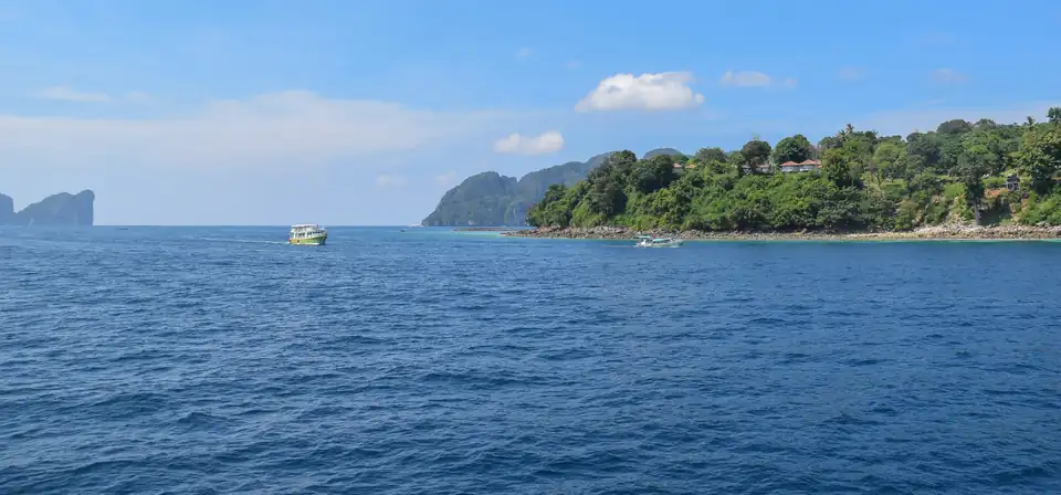 A passenger ferry approaching the forested limestone coast of Koh Phi Phi Don over deep blue water