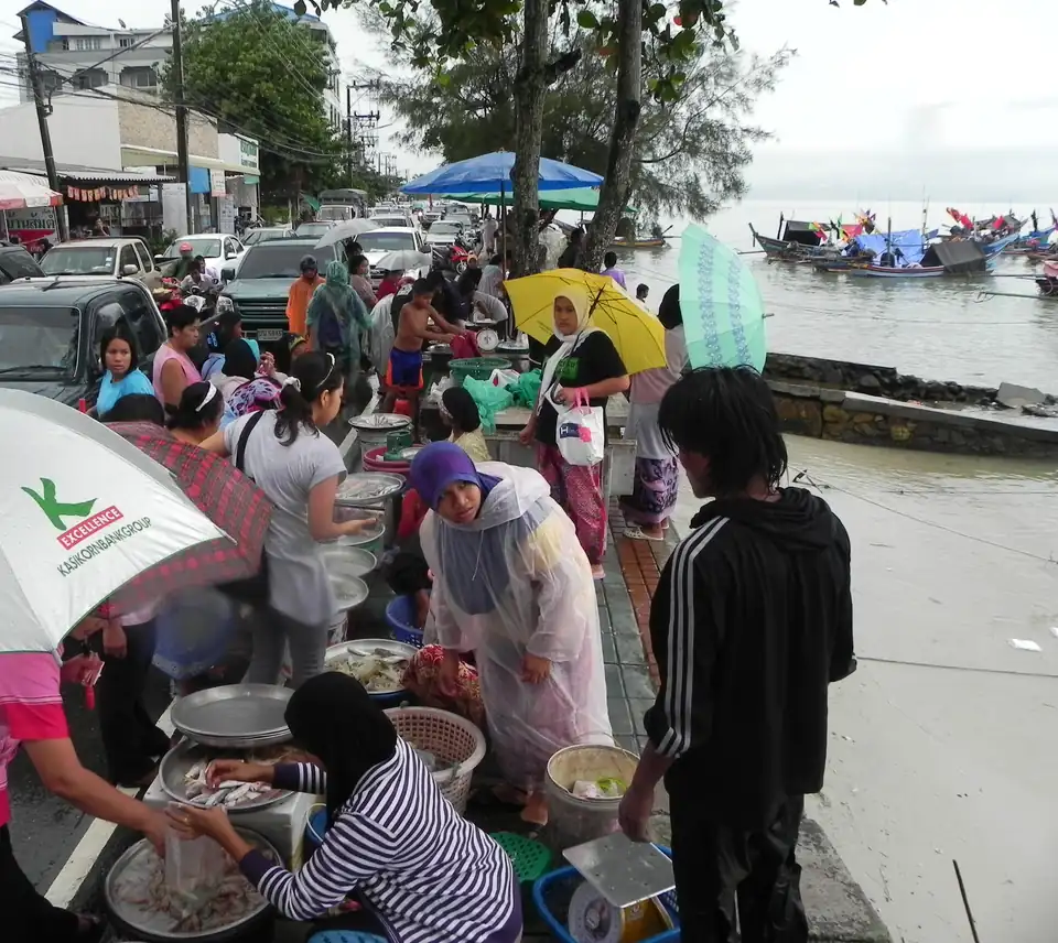 Women selling fish from bowls on the seafront pavement at Nathon under umbrellas, with fishing boats moored behind