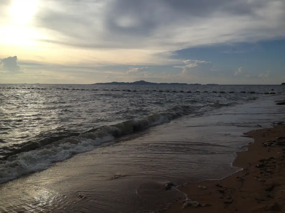 Sunset over the water at Jomtien beach with the hills of Koh Larn on the horizon and a line of swimming markers