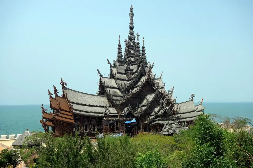 The Sanctuary of Truth, a tall carved wooden building with tiered roofs and hundreds of figures, standing on the sea at Naklua