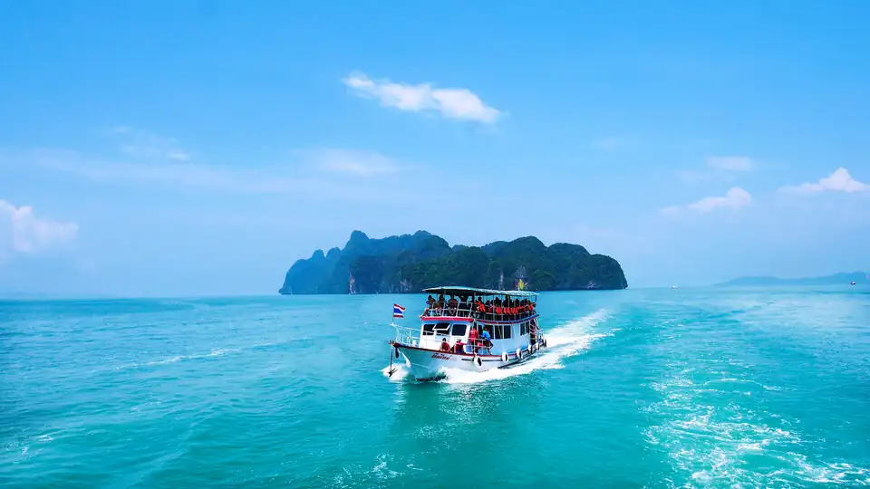 A tour boat crossing Phang Nga bay towards a limestone island