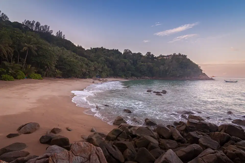 Banana Beach at first light, with boulders on the sand and two long-tails offshore