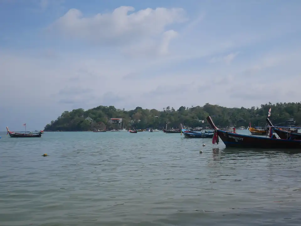 A fleet of long-tail boats moored off Rawai with the green headland behind