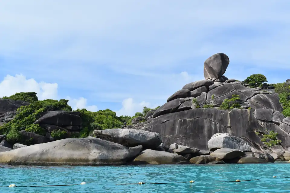 A balanced granite boulder on the headland above Donald Duck Bay, with turquoise water and a mooring line below