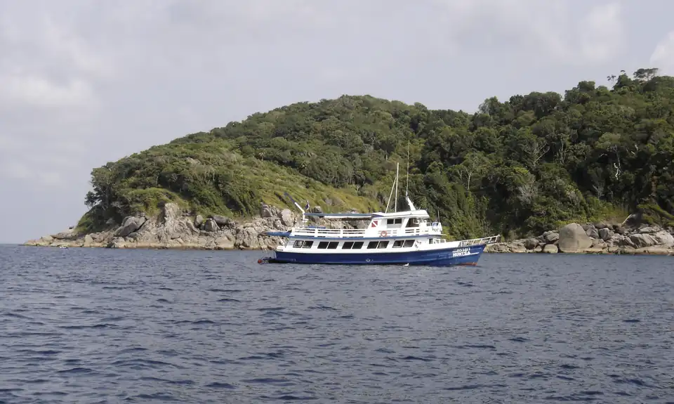 A liveaboard dive boat at anchor in a bay below a forested granite headland