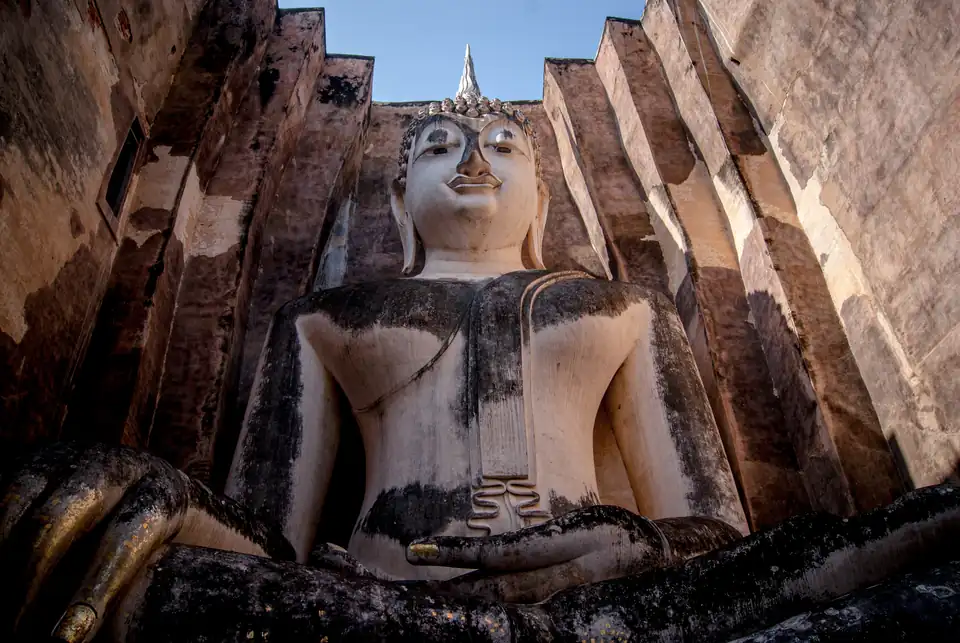An enormous seated Buddha filling a roofless brick chamber, seen from below with the walls closing in