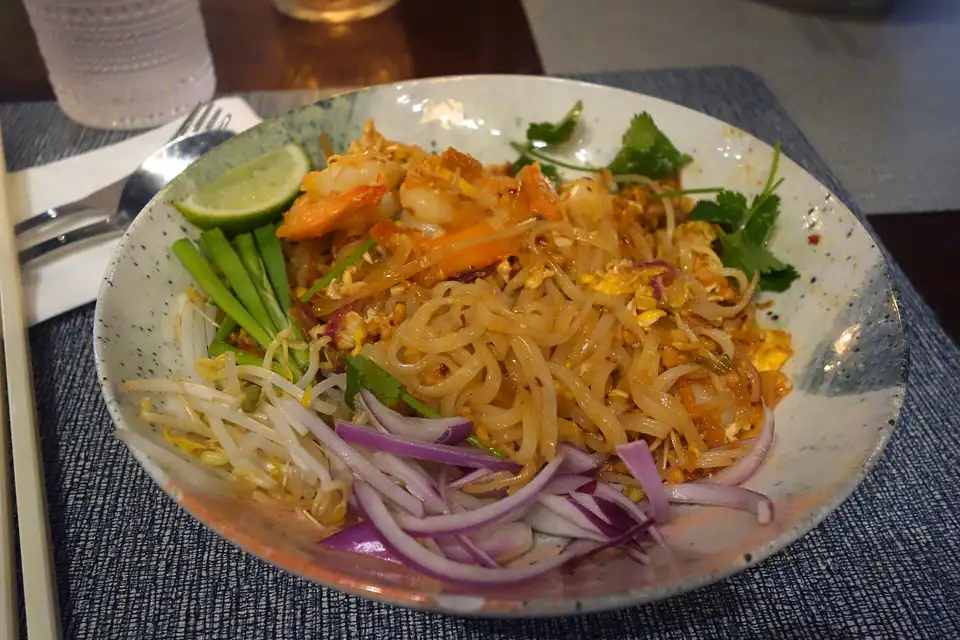 A plate of pad thai with lime, bean sprouts and peanuts