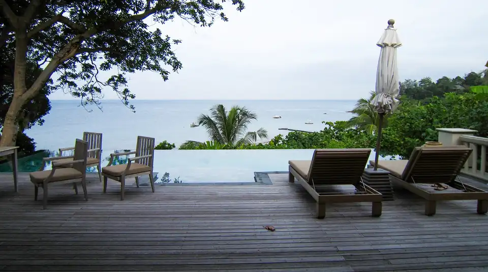 An empty pool villa terrace with loungers and a folded parasol above a calm sea