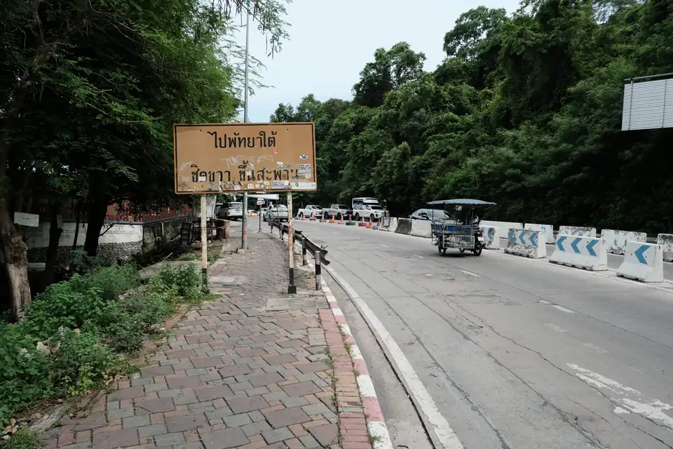 A roadside in Thailand with a directional sign in Thai and a tuk-tuk