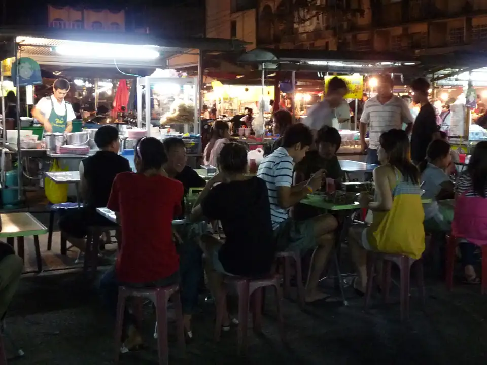 Diners on plastic stools at food stalls in Trat's night market at night, all of them Thai
