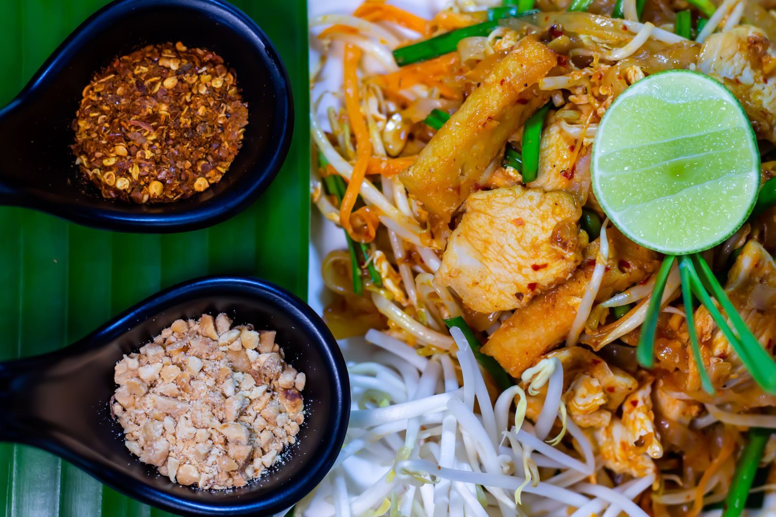 A plate of pad thai with lime, bean sprouts and peanuts